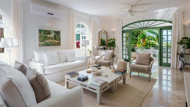A spacious living room with a white sofa, a coffee table, and a view of a lush garden through a green archway. - Sugar Hill - Jade Vine 3 Bedroom Villa (Holetown)