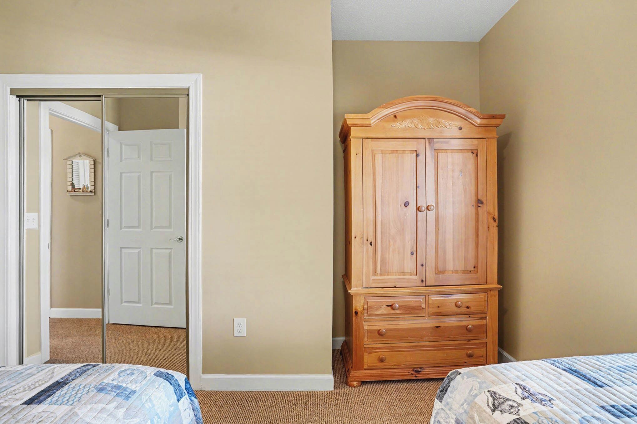 A bedroom with a wooden wardrobe, a bed with a patterned bedspread, and a door leading to another room.