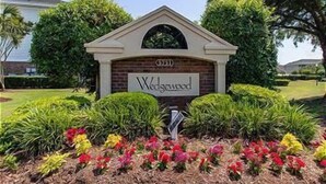 Placa para 'Wedgewood', com um arco de tijolos e um pequeno jardim com flores coloridas na frente.