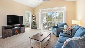 Uma sala de estar com televisão, lareira, sofá e varanda com vista.