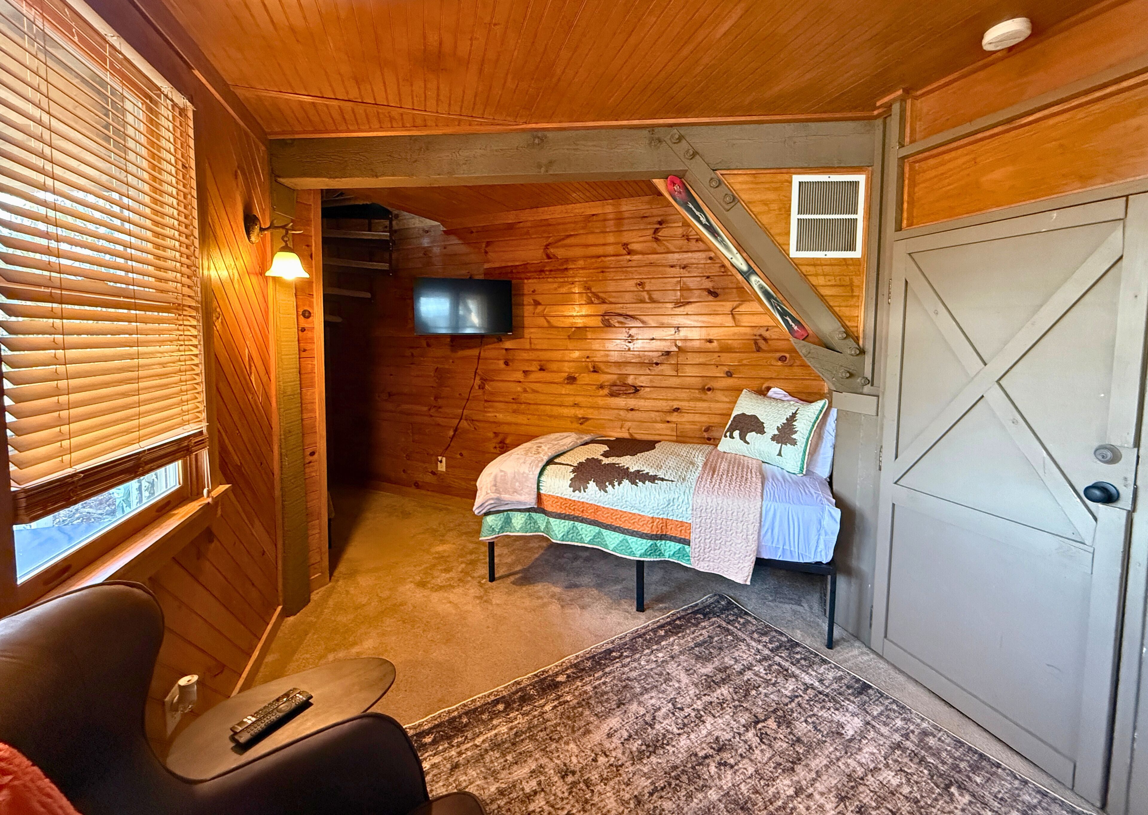 Una stanza accogliente di una baita con un letto, una televisione e una poltrona.