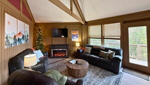 Ein gemütliches Wohnzimmer mit Kamin, Ledersofas, einem Weihnachtsbaum und einem großen Fenster mit Jalousien.