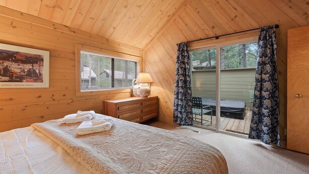 Une chambre confortable dans un chalet en bois, avec un grand lit, une commode, une lampe et une porte-fenêtre coulissante donnant sur un patio.
