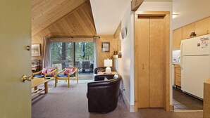 Un intérieur chaleureux avec des murs en bois, un coin repas avec des chaises, une cuisine équipée d’un réfrigérateur et une porte-fenêtre coulissante donnant sur un espace extérieur.