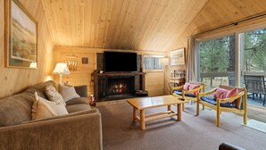 L'intérieur d'un chalet accueillant, avec un plafond en bois, une cheminée, un canapé, une table basse et une vue magnifique à travers de grandes fenêtres.