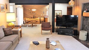 A living room with a sofa, a coffee table with remotes, a TV, and a fireplace. - Meadow House 58 2 Bedroom Home (Bend)