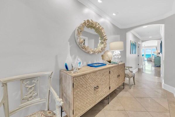 A hallway with a decorative mirror, a lighted lamp, and a wooden cabinet with a peacock design. - Adagio C-201 Beach Front 4/3 - NEW to program for 2026! (Santa Rosa Beach)
