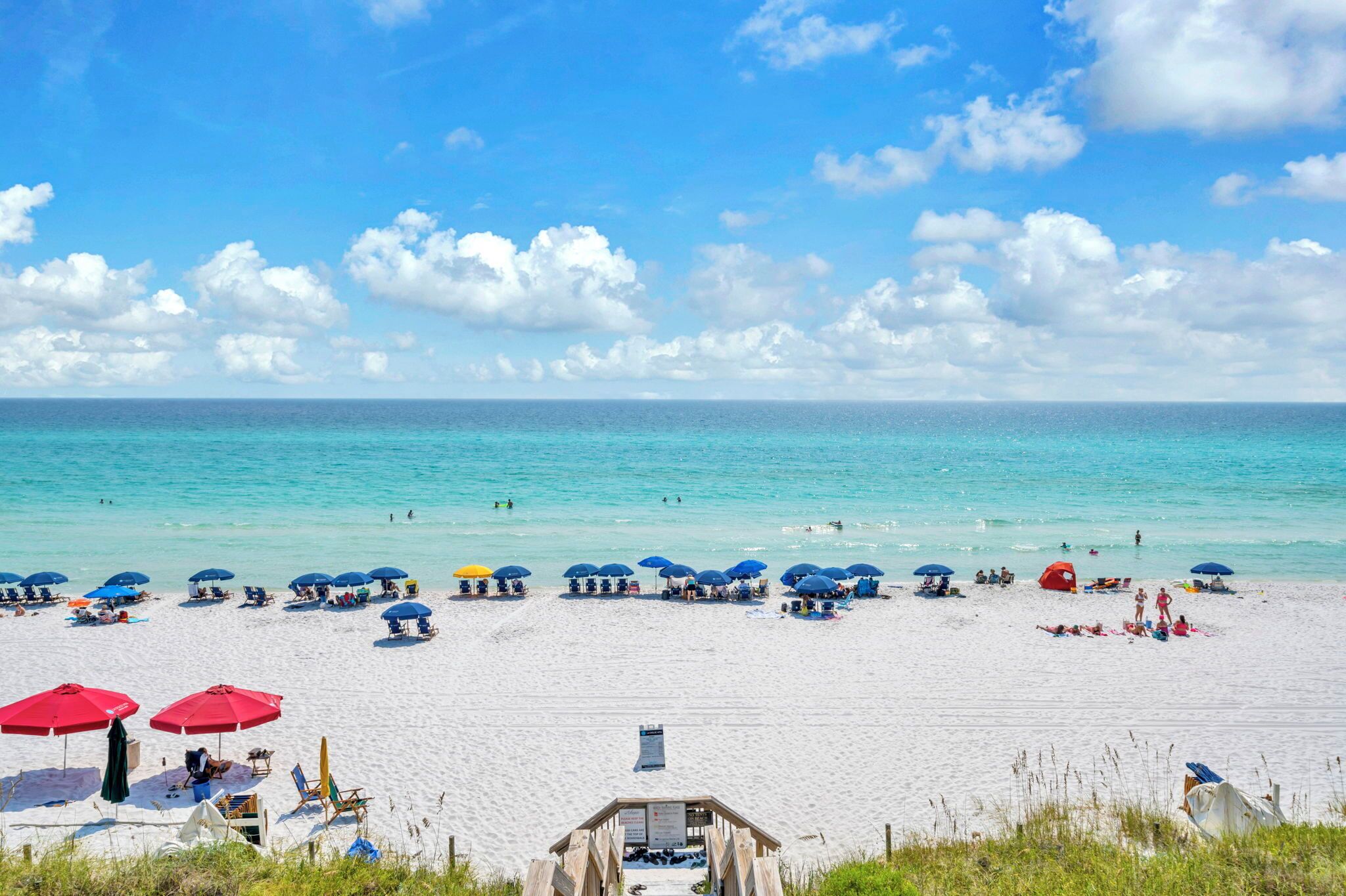 A beach with umbrellas and beach chairs, a wooden structure, and the ocean in the background.