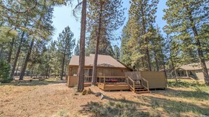 A cabin with a deck, surrounded by tall pine trees. - Tamarack 8 3 Bedroom Home (Bend)