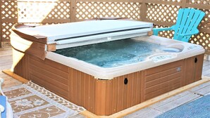 Un bain à remous doté d’un couvercle, entouré d’une terrasse en bois et d’une clôture à treillis.