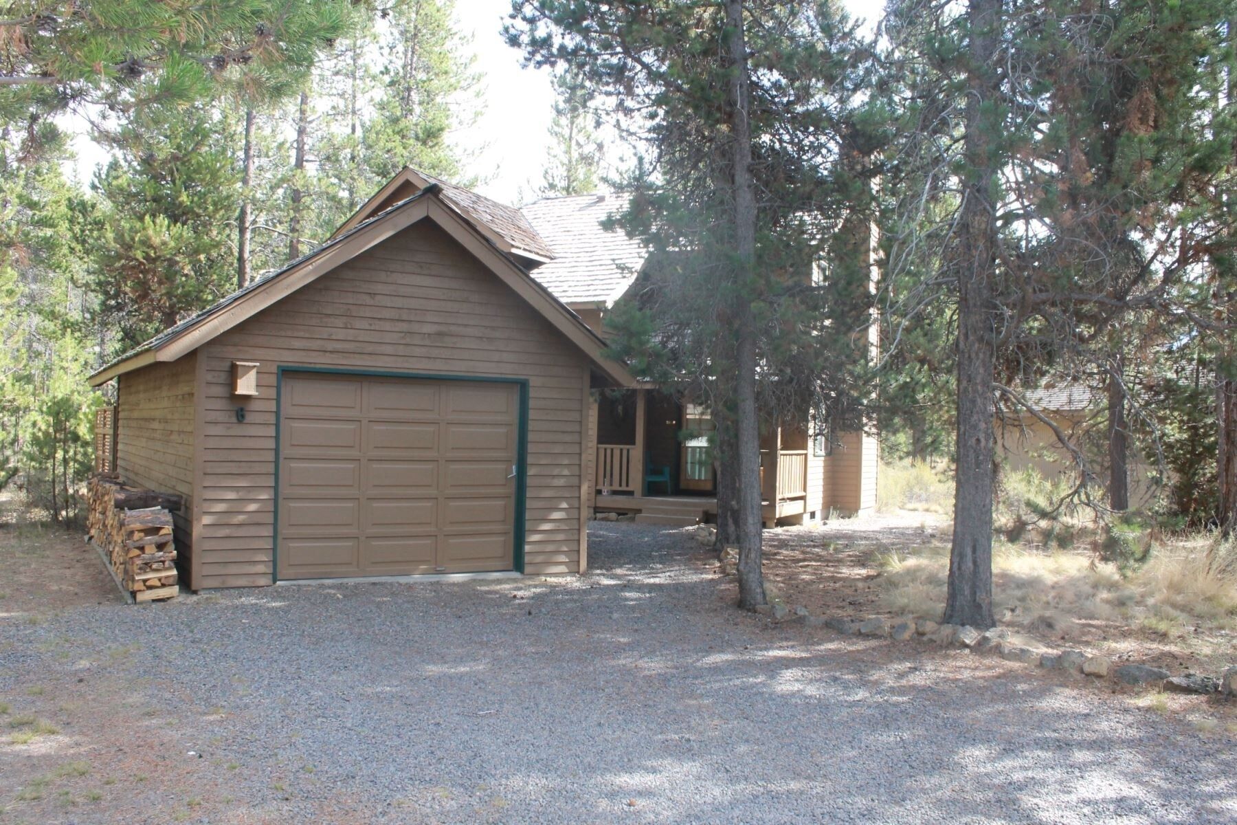 A single-story wooden cabin with a large garage door, surrounded by trees.