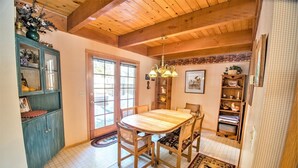 Un coin repas avec une table et des chaises en bois, un lustre et une vue sur l’extérieur par une porte vitrée.
