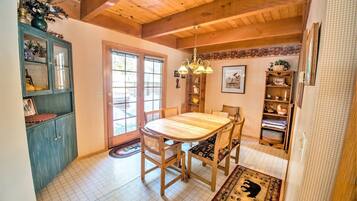 A dining area with a wooden table and chairs, a chandelier, and a view through a glass door to the outside.