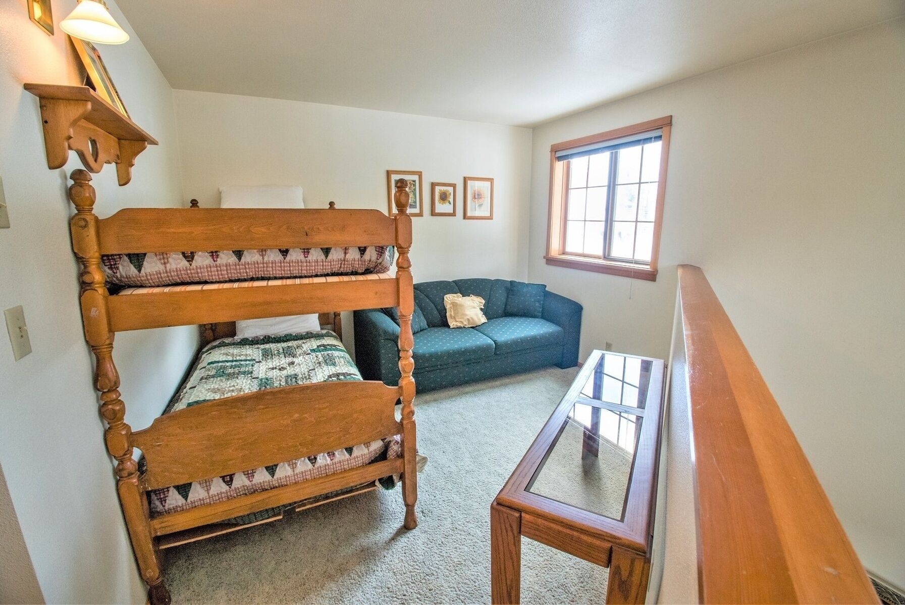 A room with a wooden bunk bed, a blue sofa, a small table, and a window with blinds.