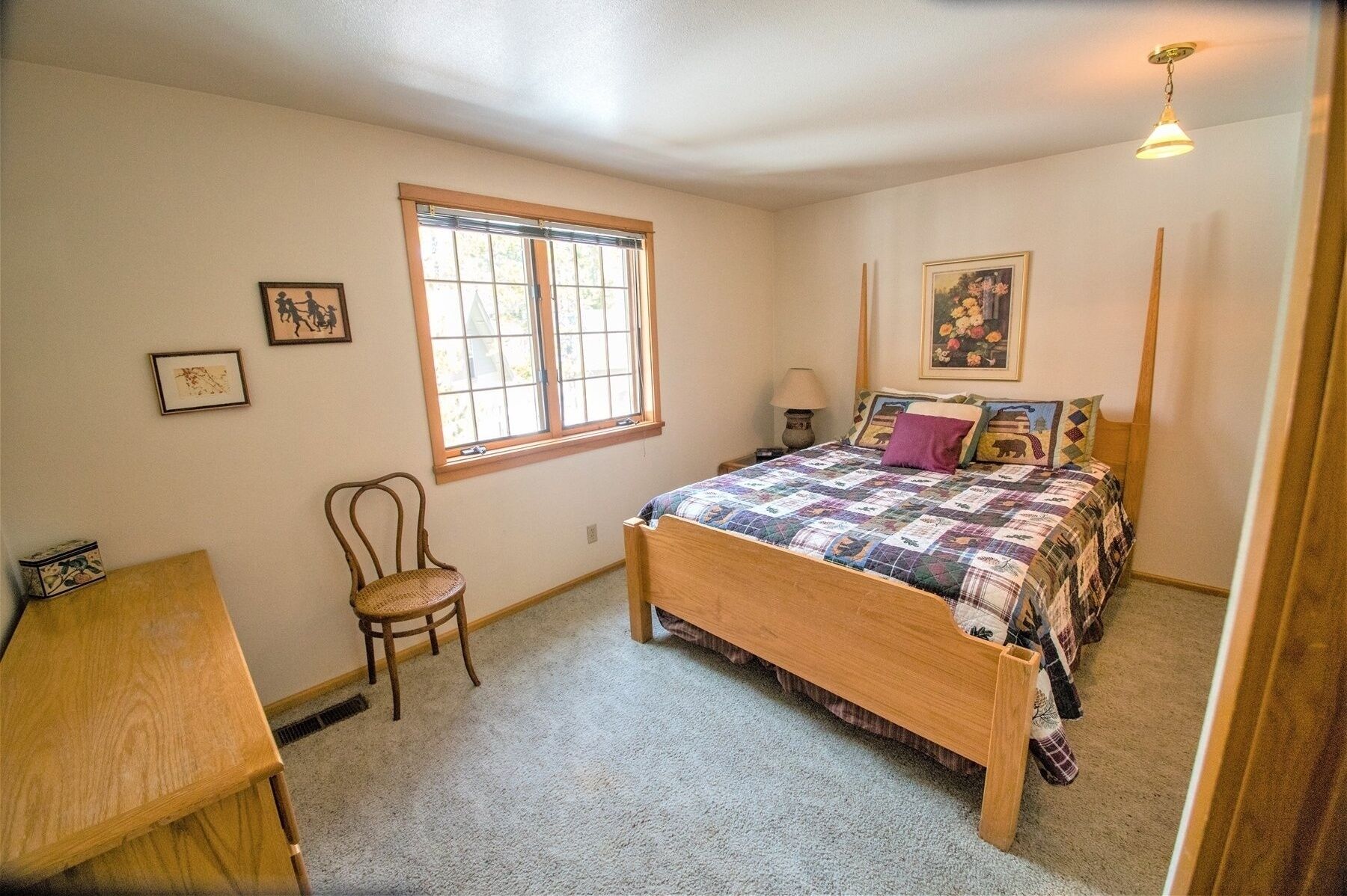 A bedroom with a wooden bed, a chair, a desk, a window, and a lamp.