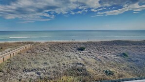 Ein Strand mit einem hölzernen Steg, der zum Ufer führt, Sanddünen und einem klaren Himmel.