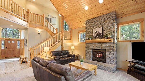 Ein geräumiges Wohnzimmer mit Kamin aus Stein, Ledersofas, einer Holztreppe und einem großen Fernseher.