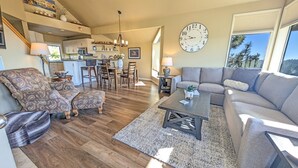 A spacious living room with a sofa, two armchairs, a coffee table, and a dining area with chairs and a table. A large wall clock is visible, and there is a view of the outdoors through a window. - Mt Bachelor Village 424 A Sr 2 Bedroom Condo (Bend)