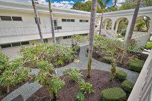 A courtyard with palm trees, a covered walkway, and a building with multiple windows and balconies. - Sunset on Third – top floor 2BR/2BA Condo Steps from the Gulf & 5th Ave (Naples)