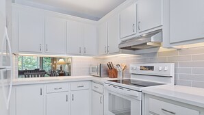 Een moderne keuken met witte kastjes, een inbouwmagnetron, een fornuis en een raam met uitzicht op een tuin.