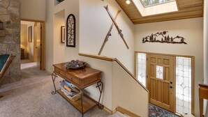 A staircase with a wooden railing, a stone wall, a wooden table with decorative items, and a door with frosted glass panels. - Lark 4 2 Bedroom Home (Bend)
