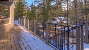 A wooden deck with a metal railing, surrounded by snow-covered ground and trees. - Lark 4 2 Bedroom Home (Bend)