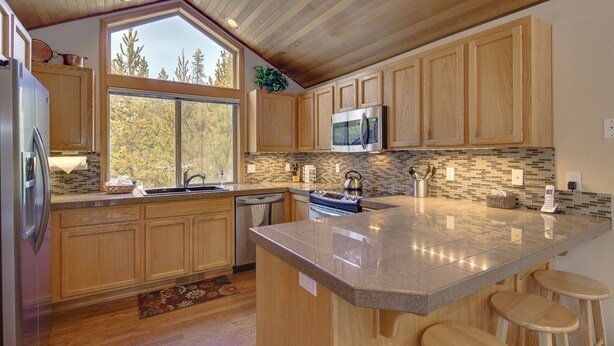 A modern kitchen with wooden cabinets, a large island with stools, a stainless steel refrigerator, and a microwave. - Lark 4 2 Bedroom Home (Bend)