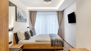 Ein modernes Schlafzimmer mit einem Bett, Nachttischen aus Holz, einem an der Wand montierten Fernseher und einem Gemälde.