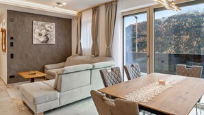 Ein modernes Wohnzimmer mit einer Couch, einem Esstisch und einem großen Fenster mit Blick auf die Berge.