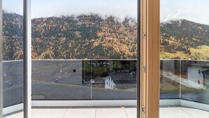 Ein Balkon mit Blick auf einen bewaldeten Berg und ein kleines Gebäude in der Ferne.