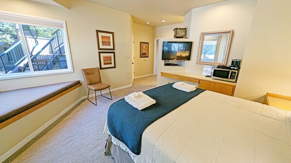 A hotel room with a bed, a chair, a TV, a microwave, and a window with a view of a staircase. - Mt Bachelor Village 328 B 1 Bedroom Condo (Bend)