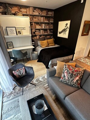 A modern living room with a sofa, armchair, and a bed with a dark blanket. There is a bookshelf filled with books and a framed picture on the wall. - Stunning studio with ocean view (Kristiansand)