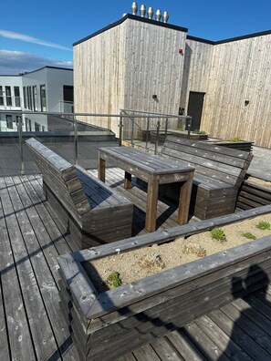 A rooftop deck with wooden benches and a table, surrounded by a wooden railing. - Stunning studio with ocean view (Kristiansand)