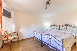 Ein Schlafzimmer mit Bett, Sessel, Wandfernseher und Deckenleuchte.