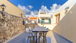 A patio with a table and chairs, stone wall, and buildings in the background. - Casa Carolina with Private Terrace, Wi-Fi and Air Conditioning (Pozzallo)