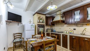 A kitchen with wooden cabinets, a dining table with chairs, a refrigerator, and a television mounted on the wall. - Casa Carolina with Private Terrace, Wi-Fi and Air Conditioning (Pozzallo)