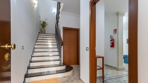 A staircase leading to a room with a wooden door, a fire extinguisher, and a potted plant. - Casa Carolina with Private Terrace, Wi-Fi and Air Conditioning (Pozzallo)