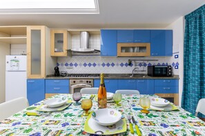 A modern kitchen with blue cabinets, a microwave, a stove, and a dining table set with plates, glasses, and cutlery. - Casa Carolina with Wi-Fi and Air Conditioning (Pozzallo)