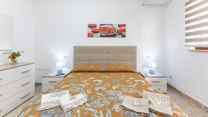 Ein Schlafzimmer mit Bett, Nachttischen, Ablagefläche und einer Wand-Klimaanlage, sowie einem Fenster mit Jalousien.