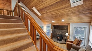 A wooden staircase leading to a living area with a stone fireplace, a sofa, and a window with blinds. - Sequoia 14 2 Bedroom Home (Bend)