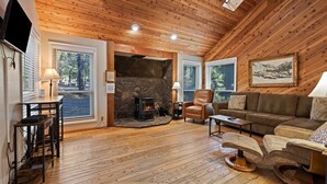 A cozy living room with a stone fireplace, leather armchair, and a large painting on the wall. - Sequoia 14 2 Bedroom Home (Bend)
