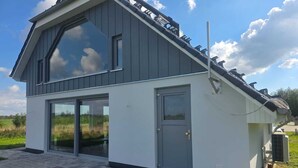 Ein modernes, zweistöckiges Haus mit einem großen Glasfenster, einer grauen Tür und einem Solarmodul auf dem Dach.