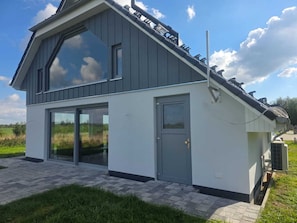 Una casa moderna de dos pisos con un amplio ventanal, una puerta gris y un panel solar en el techo.