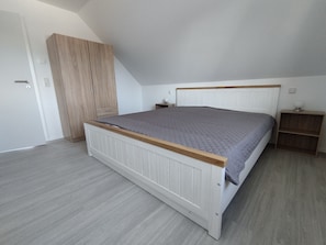 Un dormitorio con cama, armario, mesita de noche y estante.