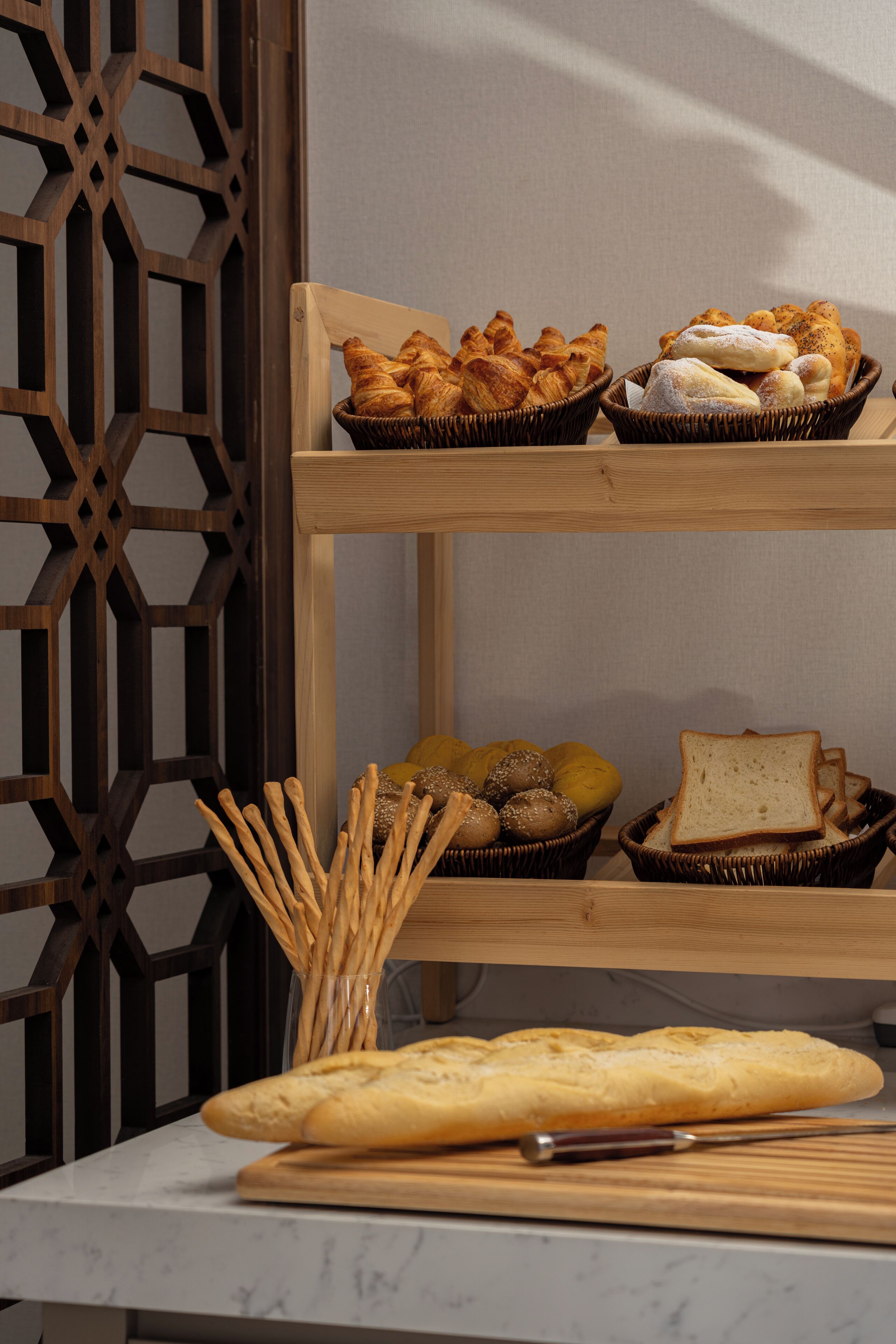A wooden display stand with baskets containing bread and pastries, a cutting board with a knife, and a decorative wooden partition.