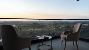 Un balcón con dos sillas y una mesita, con vista a un paisaje urbano que incluye edificios y un parque.