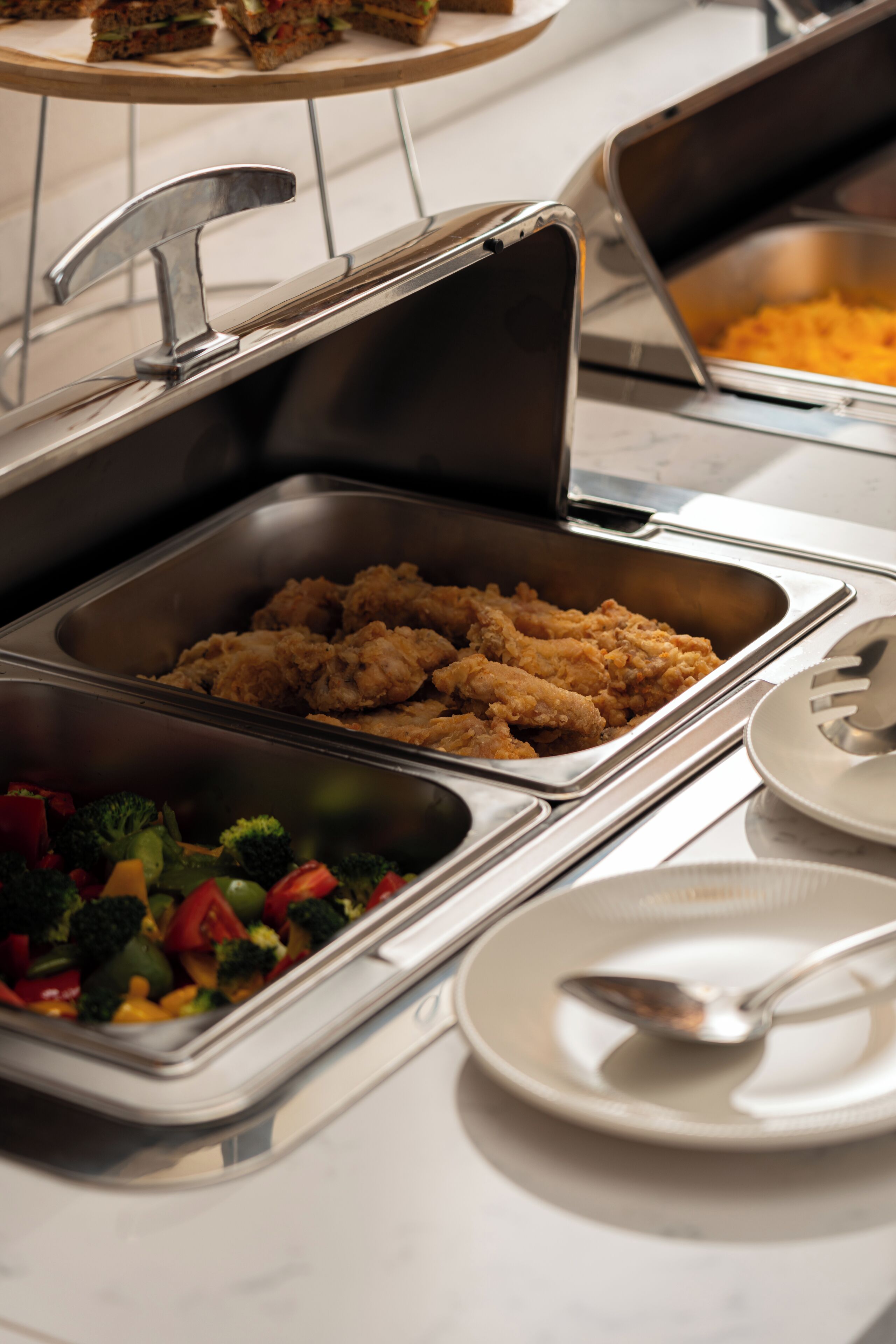A buffet setup with various food items including fried chicken, vegetables, and a casserole dish.