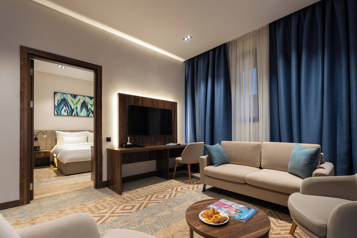 Une chambre d’hôtel avec un lit, un bureau avec une télévision, un canapé et une table basse avec un magazine et des croissants.