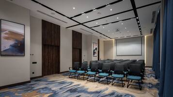 A conference room with rows of chairs, a projector screen, and a large abstract painting on the wall.