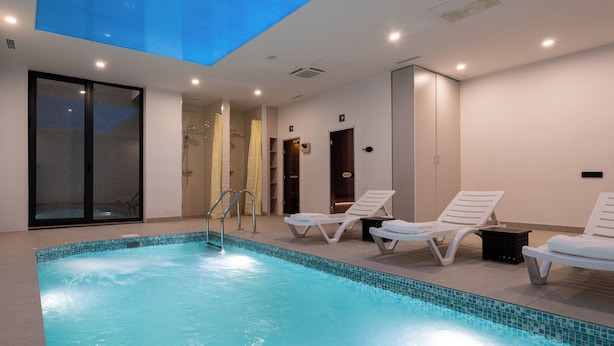 Una piscina interior con tragaluces, dos sillones de descanso y una zona de ducha.
